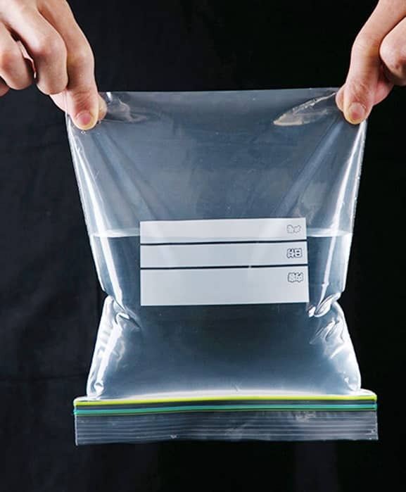 Hand holding ziplock bag hald filled with water.